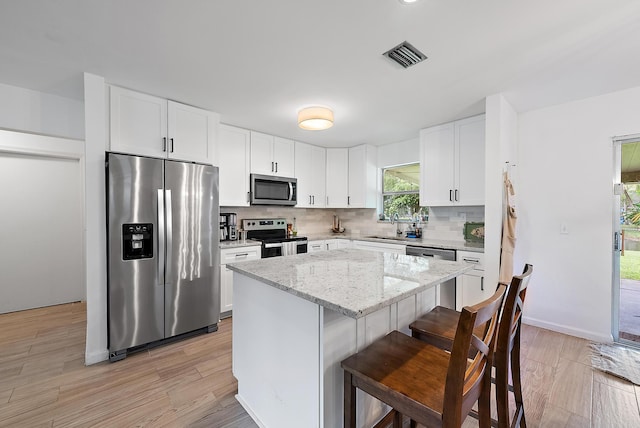 kitchen with appliances with stainless steel finishes, backsplash, light stone counters, light hardwood / wood-style flooring, and a center island