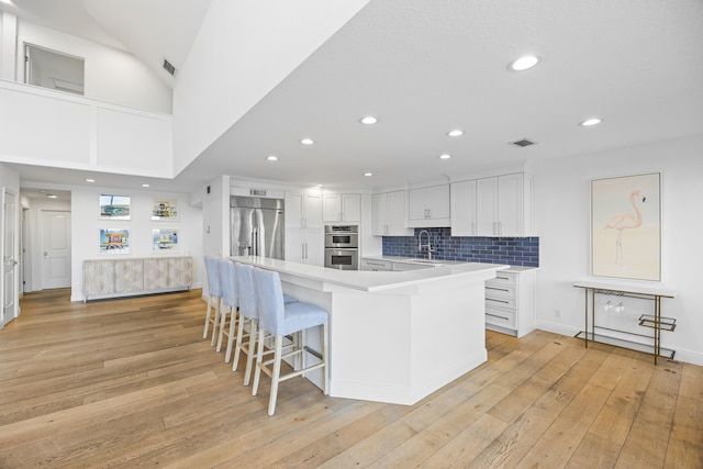 kitchen with white cabinetry, a kitchen breakfast bar, light hardwood / wood-style flooring, backsplash, and appliances with stainless steel finishes