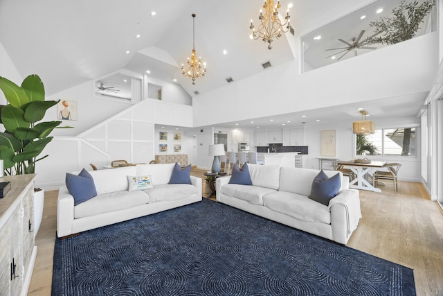 living room featuring high vaulted ceiling, ceiling fan with notable chandelier, and light wood-type flooring