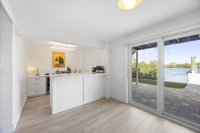 kitchen with light hardwood / wood-style floors, white cabinetry, kitchen peninsula, and beverage cooler