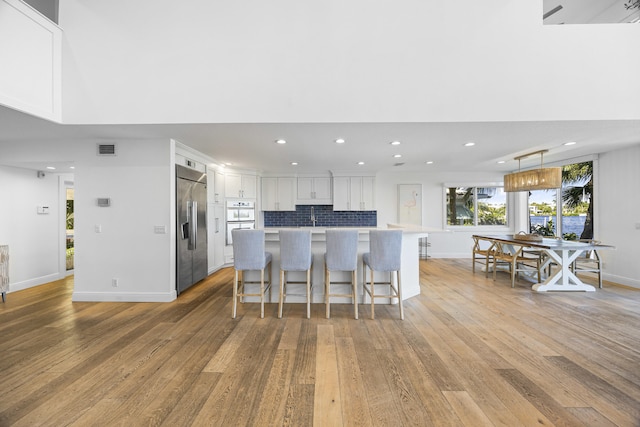 kitchen featuring white cabinetry, a kitchen breakfast bar, built in fridge, light hardwood / wood-style floors, and decorative light fixtures