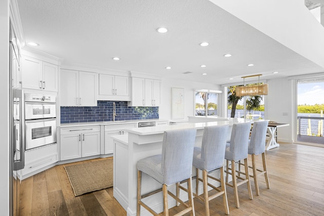 kitchen featuring double oven, sink, a center island with sink, light hardwood / wood-style flooring, and white cabinets