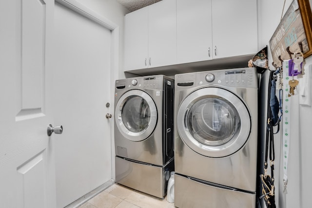 washroom featuring cabinets, a textured ceiling, light tile patterned flooring, and washing machine and clothes dryer