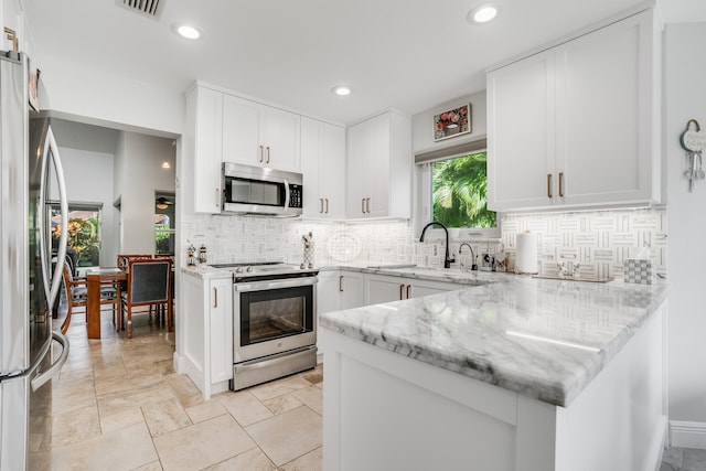 kitchen with white cabinets, decorative backsplash, stainless steel appliances, and light stone countertops