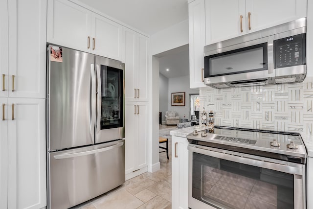 kitchen with white cabinets, appliances with stainless steel finishes, tasteful backsplash, and light stone counters