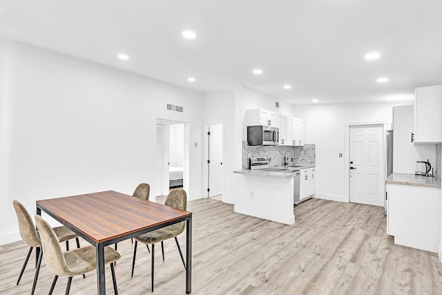 kitchen featuring backsplash, stainless steel appliances, sink, light hardwood / wood-style flooring, and white cabinetry