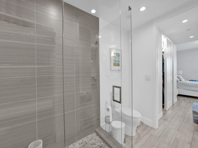 bathroom featuring a tile shower, toilet, and wood-type flooring