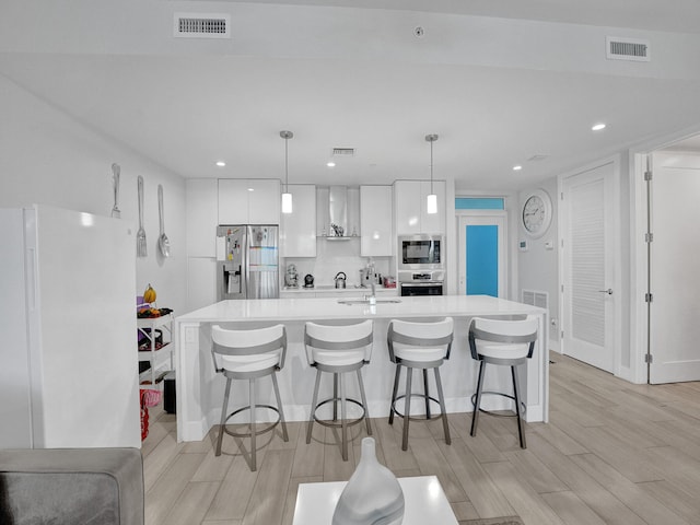 kitchen featuring light hardwood / wood-style flooring, white cabinets, a kitchen bar, hanging light fixtures, and appliances with stainless steel finishes