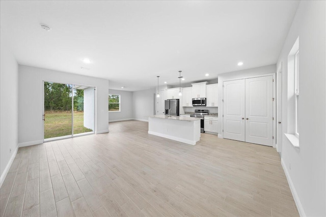 kitchen featuring light hardwood / wood-style floors, hanging light fixtures, a kitchen island with sink, white cabinetry, and appliances with stainless steel finishes