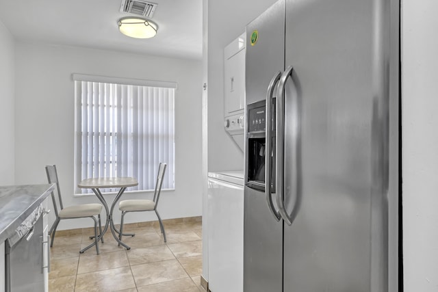 kitchen with light tile patterned flooring, stainless steel refrigerator with ice dispenser, and stacked washer and clothes dryer