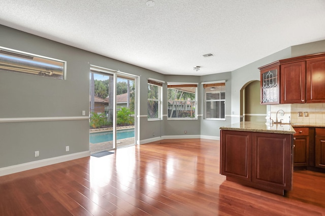 kitchen with decorative backsplash, light stone countertops, wood-type flooring, and a textured ceiling