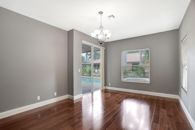 spare room featuring dark wood-type flooring, a textured ceiling, an inviting chandelier, and plenty of natural light