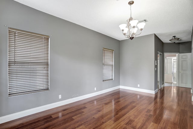 spare room featuring a textured ceiling, hardwood / wood-style flooring, and an inviting chandelier