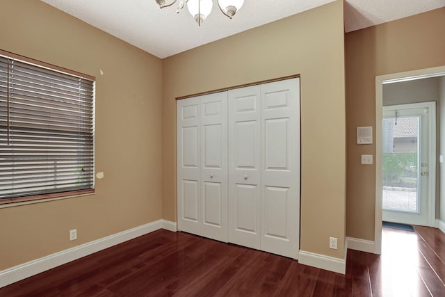 unfurnished bedroom featuring dark hardwood / wood-style flooring, a textured ceiling, a chandelier, and a closet