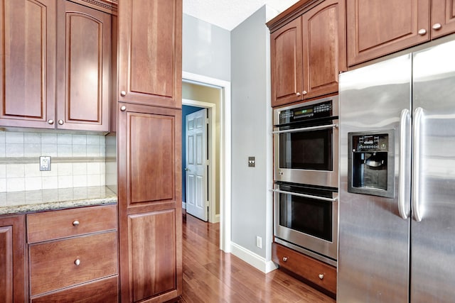 kitchen featuring stainless steel appliances, light stone counters, a textured ceiling, backsplash, and dark hardwood / wood-style flooring