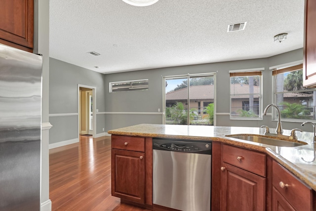 kitchen with a textured ceiling, appliances with stainless steel finishes, sink, and light hardwood / wood-style flooring