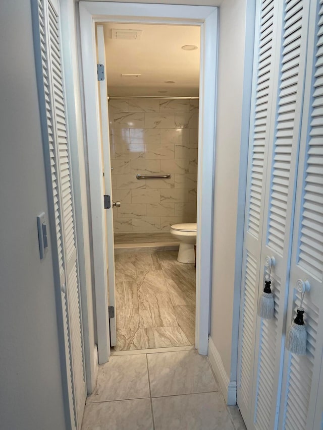 bathroom with a tile shower, toilet, and tile patterned floors