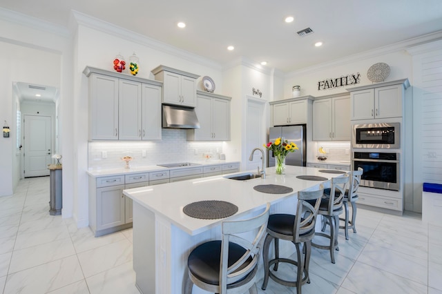 kitchen with a kitchen bar, ventilation hood, stainless steel appliances, a kitchen island with sink, and sink