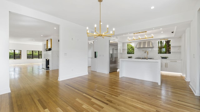 kitchen with pendant lighting, light hardwood / wood-style flooring, built in refrigerator, white cabinets, and wall chimney exhaust hood