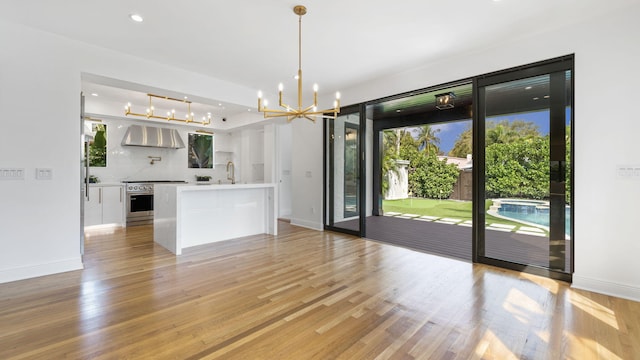 kitchen with pendant lighting, white cabinetry, a center island with sink, wall chimney range hood, and light wood-type flooring