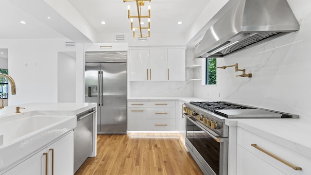 kitchen with exhaust hood, light stone counters, high quality appliances, pendant lighting, and white cabinets