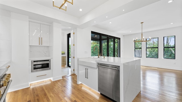 kitchen with white cabinetry, sink, appliances with stainless steel finishes, hanging light fixtures, and light hardwood / wood-style flooring