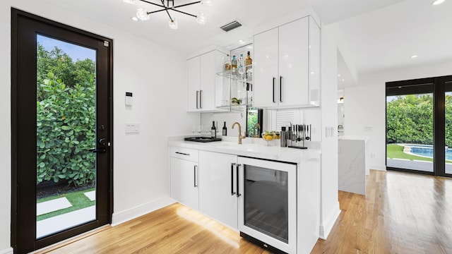 bar with light hardwood / wood-style floors, beverage cooler, and white cabinets