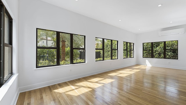 unfurnished room with a healthy amount of sunlight, a wall unit AC, and light hardwood / wood-style floors