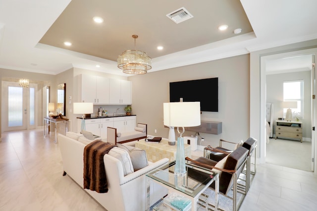 living room featuring a tray ceiling, crown molding, french doors, and a chandelier