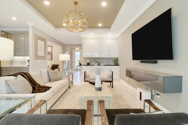 living room with a tray ceiling, an inviting chandelier, and ornamental molding