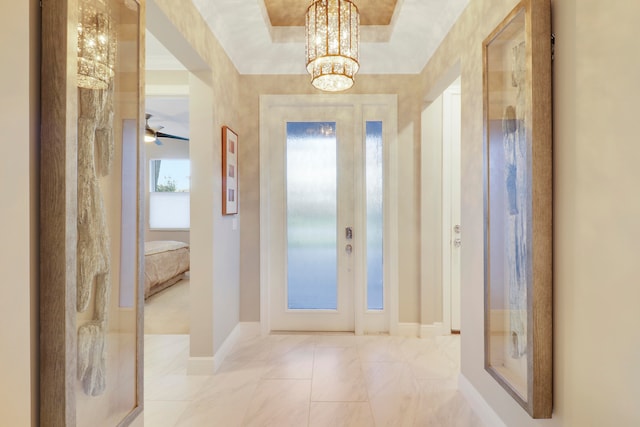 foyer entrance with ceiling fan with notable chandelier and a raised ceiling