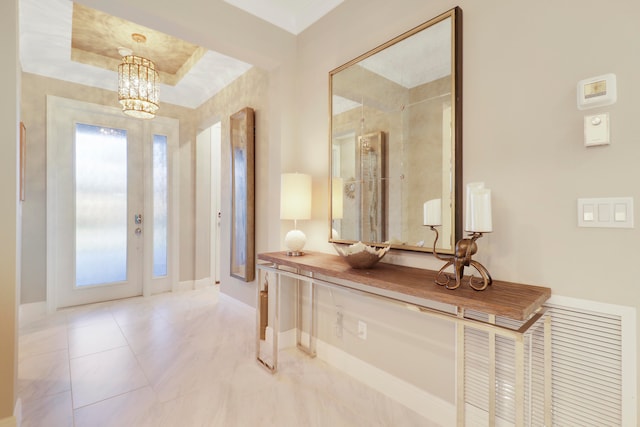 entrance foyer with light tile patterned floors, a raised ceiling, and a notable chandelier