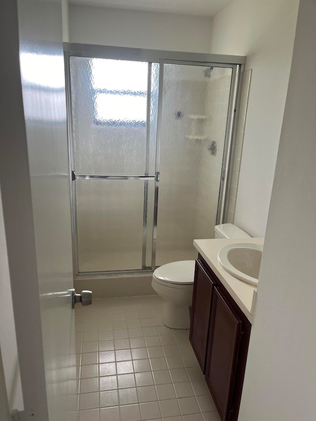 bathroom featuring tile patterned flooring, vanity, toilet, and a shower with door