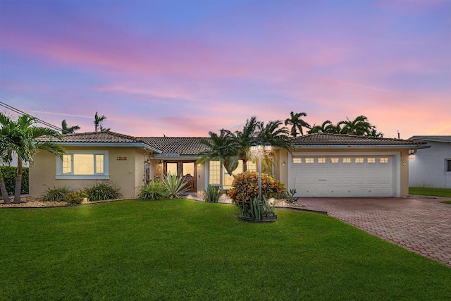 ranch-style house with an attached garage, a yard, a tiled roof, decorative driveway, and stucco siding