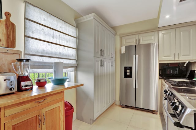 kitchen featuring wooden counters, appliances with stainless steel finishes, white cabinetry, and light tile patterned flooring