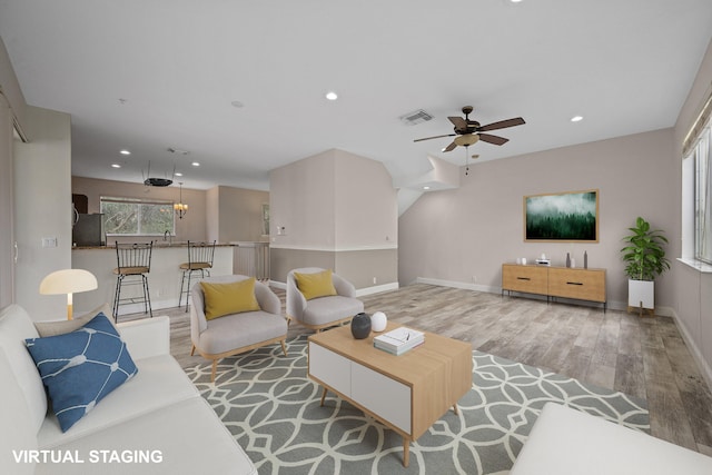 living room with ceiling fan with notable chandelier and light wood-type flooring