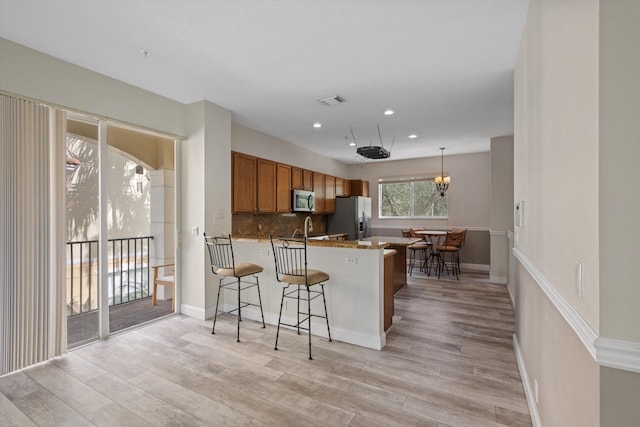 kitchen featuring kitchen peninsula, appliances with stainless steel finishes, a kitchen bar, tasteful backsplash, and light hardwood / wood-style flooring