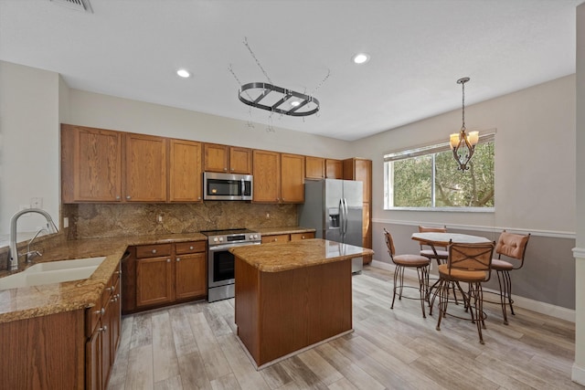 kitchen with light stone countertops, sink, hanging light fixtures, stainless steel appliances, and light hardwood / wood-style floors