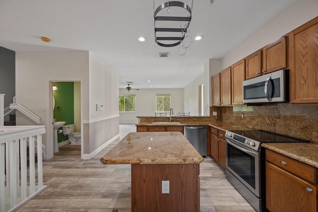 kitchen featuring decorative backsplash, appliances with stainless steel finishes, light stone counters, light hardwood / wood-style flooring, and a center island