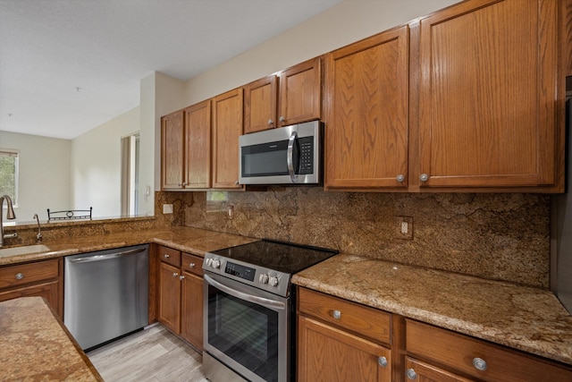 kitchen with decorative backsplash, appliances with stainless steel finishes, light wood-type flooring, light stone countertops, and sink