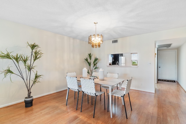 dining room with light hardwood / wood-style flooring, a textured ceiling, and an inviting chandelier