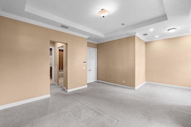 empty room with a tray ceiling, a textured ceiling, light carpet, and crown molding