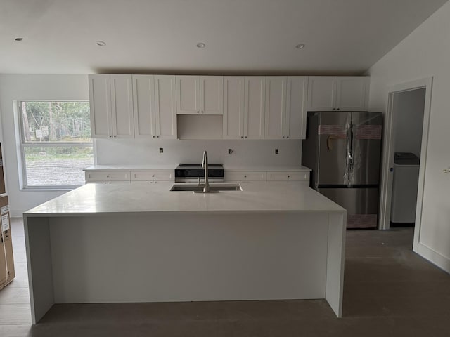 kitchen with stainless steel refrigerator, a kitchen island with sink, sink, and white cabinets