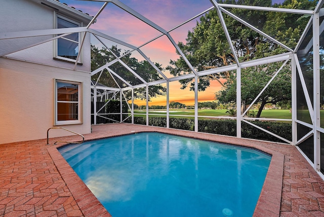 pool at dusk featuring glass enclosure and a patio area