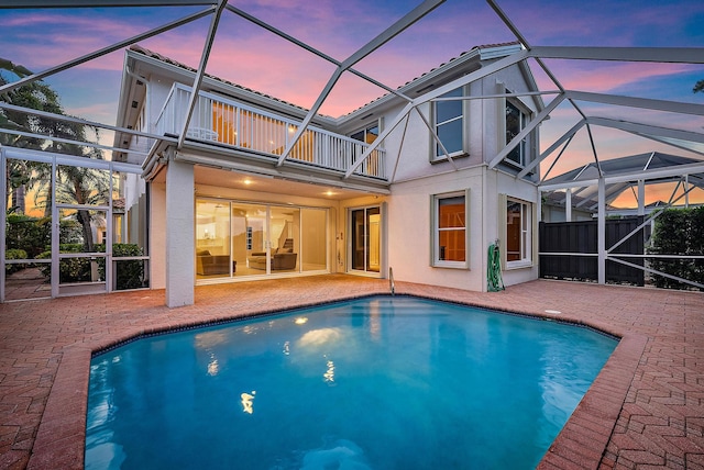 pool at dusk with glass enclosure and a patio