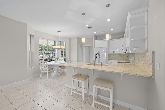 kitchen featuring stove, backsplash, light stone counters, sink, and white cabinetry