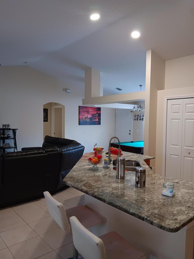 kitchen with stone counters, sink, billiards, light tile patterned floors, and a breakfast bar area