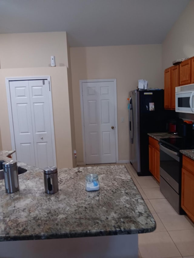 kitchen with dark stone countertops, light tile patterned floors, and appliances with stainless steel finishes