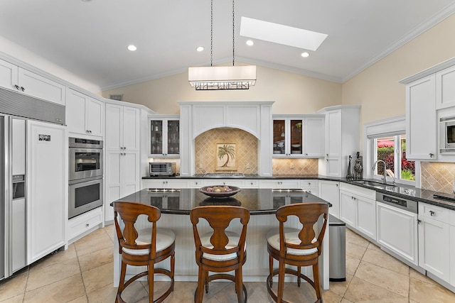 kitchen with built in appliances, a center island, ornamental molding, and vaulted ceiling with skylight