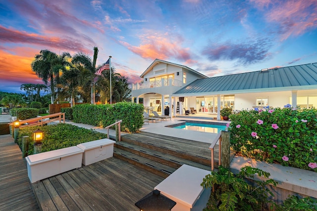 back house at dusk with a swimming pool side deck, a patio area, and a balcony